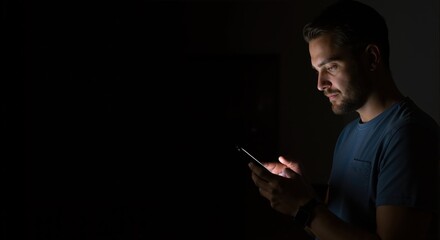 Man using a smartphone in a dark room at night. Young person's face illuminated by the glowing screen light with copy space