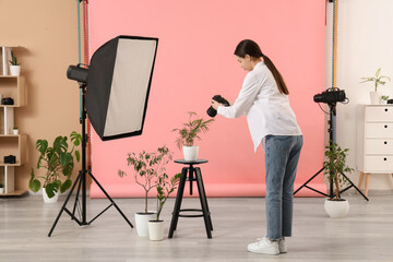 Female photographer with professional equipment, houseplants and pink backdrop in modern photo...