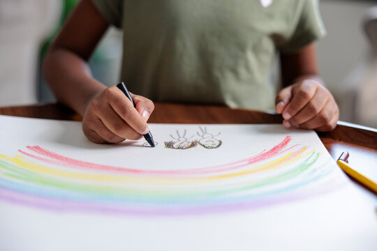 Child draws rainbow and figures with black marker.