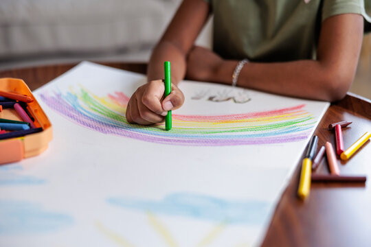 Child drawing a rainbow with crayons on white paper.
