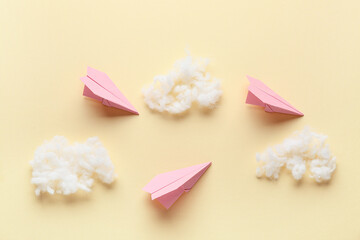 Pink paper planes with cotton wool clouds on light yellow background