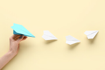 Female hand with paper planes on light yellow background