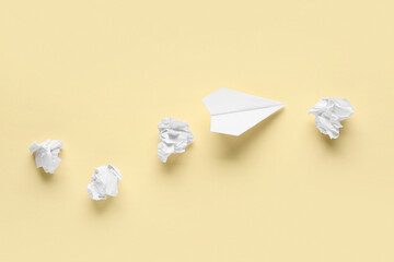 Paper plane with crumpled sheets on light yellow background