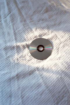Sunlight highlights a compact disc on linen sheets