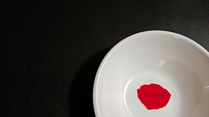 A white empty bowl with a red note reading “No Food” placed on a dark surface, representing hunger, food insecurity, poverty awareness, and the struggle for basic survival.