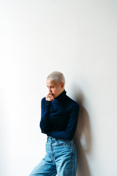 Person in Blue Turtleneck and Jeans Poses Against White Wall