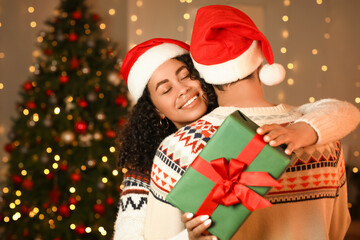 Happy young woman receiving gift from her boyfriend at home decorated for Christmas