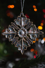 Ceramic toy in the form of a snowflake hanging on a Christmas tree with lights from a garland in the background.