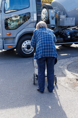 トラックの通過を待つシルバーカーを押しているおばあさん