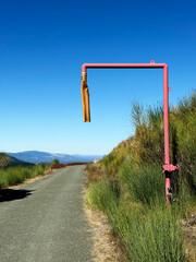 Red metal pipe beside Castillero Trail in Almaden Quicksilver County Park, California, surrounded by dry hillside vegetation, green shrubs, and clear blue sky on a sunny day