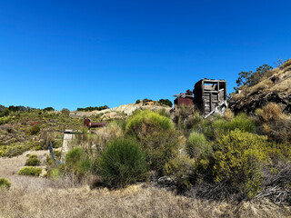 Historic rotary furnace ruins in Almaden Quicksilver County Park surrounded by dry grassland, shrubs, and rolling hills under a clear blue sky on a sunny day