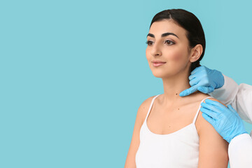 Obraz premium Dermatologist examining moles of young woman on blue background