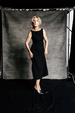 Confident woman in elegant black dress standing in studio
