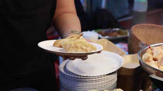 Close-up of hands exchanging Thai Baht and purchasing delicious steamed and fried dumplings at a vibrant night market in Chiang Mai, Thailand, capturing the local street food culture.