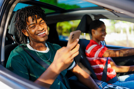 Happy man using smartphone in car with friend driving