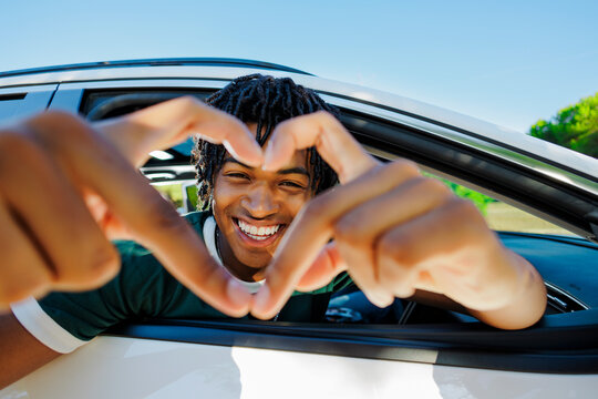 Happy man making heart shape with hands from car window