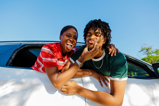 Playful couple making funny faces leaning out of car window