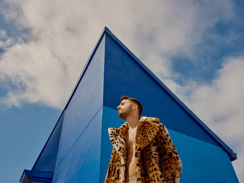 Urban Man in Leopard Coat Poses Against Blue Building Backdrop