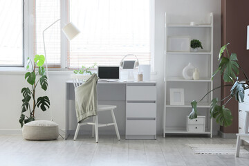 Interior of modern office with workplace, shelving unit and floor lamp near window