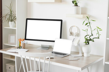 Modern workplace with computer, laptop and headphones near white wall in office