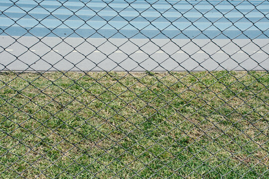Green grass and blue track behind a fence in bright sunlight