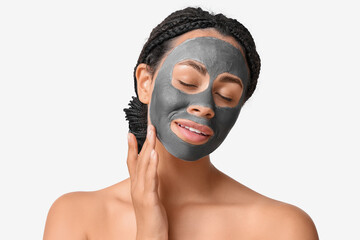 Pretty young African-American woman with activated charcoal mask on her face against white background