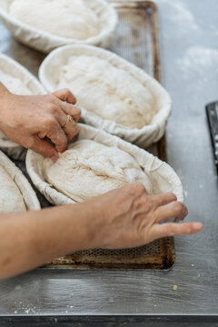 Hands adjusting bread dough in proofing baskets