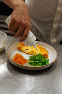 Chef plating omelette with smoked salmon and arugula