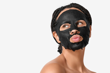 Pretty young African-American woman with activated charcoal mask on her face blowing kiss against white background