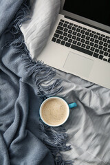 Cup of coffee with laptop and blanket on bed