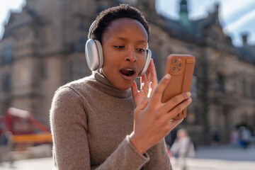 Young person enjoys music and reacts with joy while using smartphone outdoors in a lively city setting
