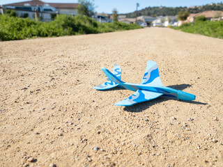 Blue Camouflage Toy Plane Resting On Dirt Path In Suburban Neighborhood
