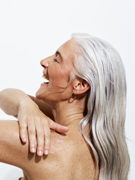 Older Woman Applies Lotion To Her Skin With Joyful Expression