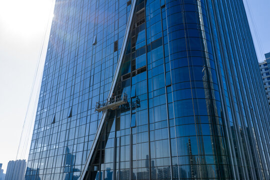 Workers on suspended platform maintaining glass facade of skyscraper