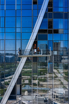 Workers on suspended platform maintaining glass facade of skyscraper