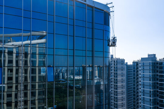 Workers on suspended platform maintaining glass facade of skyscraper