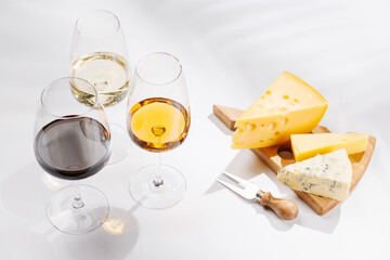 Fototapeta premium Assorted cheeses and wine glasses on white background