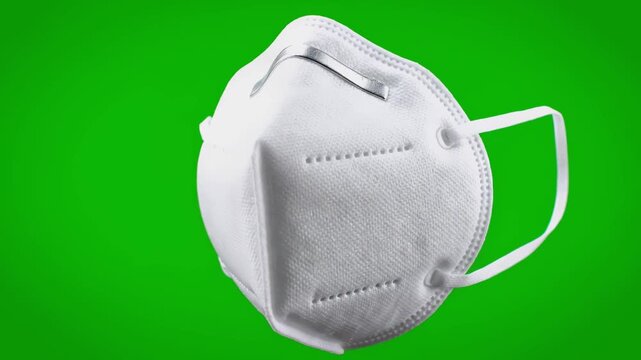 Close-up of a white, folded protective face mask with elastic straps against a green backdrop