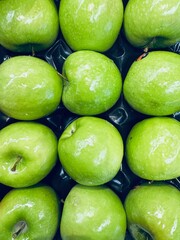 Bright, large, shiny green apples arranged in neat rows, captured in a vivid close-up
