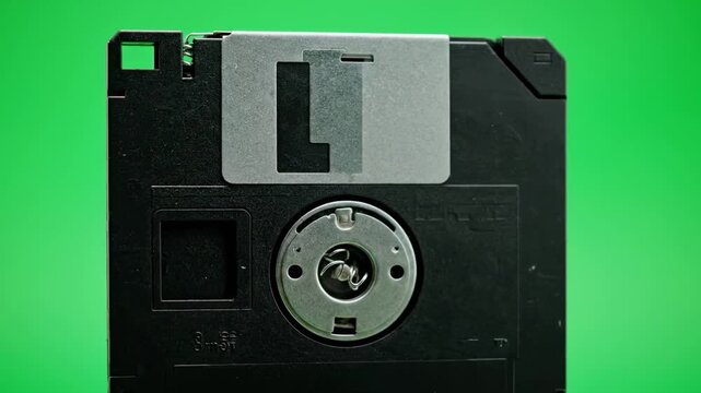 A close-up of a black floppy disk against a vibrant green backdrop, showcasing retro tech