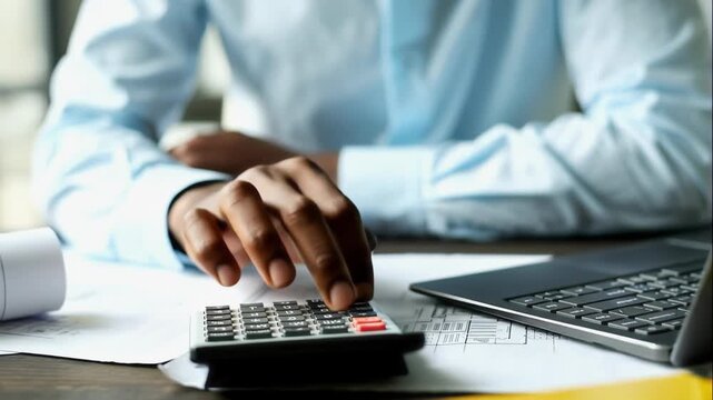 AI animated medium shot of unrecognizable black male engineer counting specifications on calculator, while working on industrial project, sitting at desk in office with laptop and technical schemes
