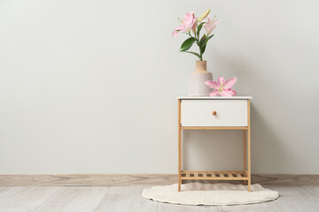 White bedside table with beautiful flowers in vase near grey wall in room
