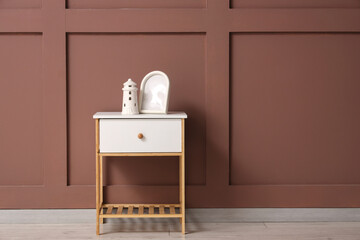 White bedside table with frame and decorative figure near brown wall in room