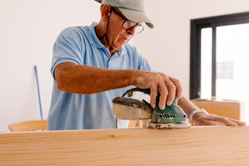 Older man polishing wooden planks with an electric sander