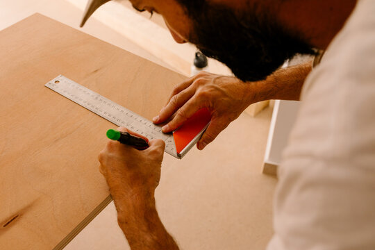 Man using a metal ruler to measure and mark a wooden board