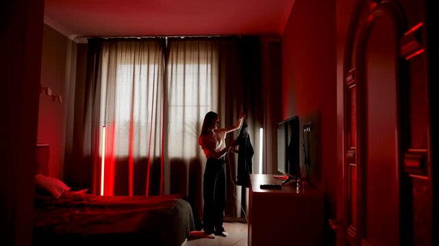 Woman ironing clothes in a softly lit room with red decor and curtains