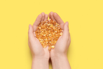 Obraz premium Female hands with vitamin E capsules on yellow background