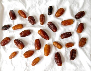Diverse varieties of dried dates randomly scattered across a white, wrinkled cloth background, showcasing a top-down view.