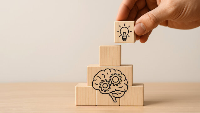 Hand placing a lightbulb block on a stack of wooden blocks with a brain and gears illustration idea innovation