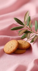 Three light brown cookies on a pink surface with an olive branch.